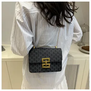 Sac bandoulière gris moderne avec imprimé M et chaîne dorée présenté dans un décor