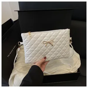 Close-up of white quilted crossbody bag featuring a gold bow accent and zip closure