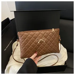 Close-up of brown quilted PU leather handbag with gold bow charm in a luxury gift box