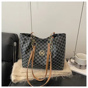 Détail d'un sac cabas noir avec imprimé M, lanières marron et ornements dorés chics