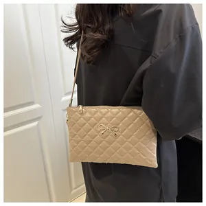 Detail view of khaki quilted crossbody bag featuring a golden bow metal accessory