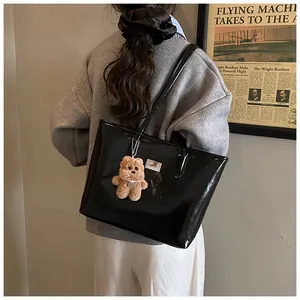 Detalle de bolso tote de cuero negro brillante con colgante de oso de peluche y correa larga