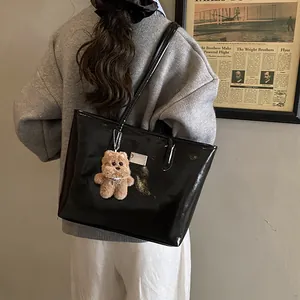 Bolso tote negro brillante con colgante de oso de peluche llevado por una modelo