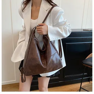 Detail of a dark brown vintage faux leather tote bag worn by a model in a white blazer
