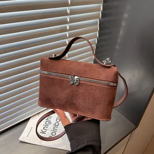 Sac boîte en daim marron avec fermetures cœur, porté main sur fond minimaliste