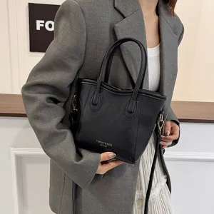 Chic black PU leather bucket bag with top handles and gold hardware on grey suit model