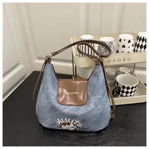 Detail of blue denim tote bag featuring cartoon patches and premium brown leather trim