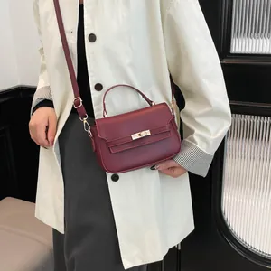 Elegant wine red leather handbag with gold metal clasp and adjustable strap for women