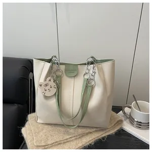 Detail of cream tote bag featuring green trim, metal chain strap and cute tiger charm