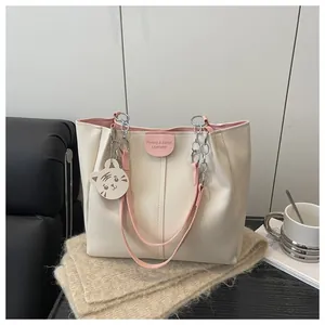 Detail of cream tote bag featuring pink straps, chain handle and cute tiger charm accessory