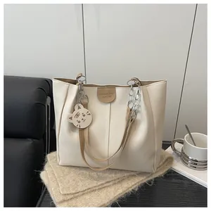 Detail of cream tote bag featuring brown leather trim and a cute cat charm accessory