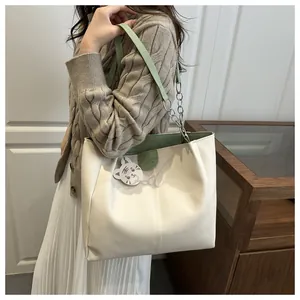 Detail of cream tote bag featuring green straps, metallic chain, and tiger charm