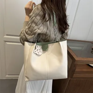 Minimalist beige tote bag with green trim and metal chain strap worn by a female model