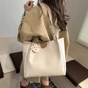 Large beige tote bag with chain strap and cat charm shown from a side view on a model