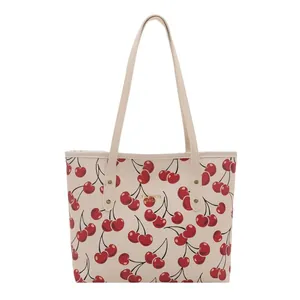 Cream tote bag with red cherry prints and thin shoulder straps, front view on plain background