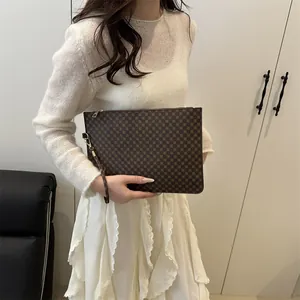 Brown monogram envelope clutch with gold zipper and wristlet shown by a model