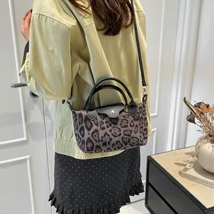 Leopard print mini tote bag with black leather handles shown on shoulder by a model
