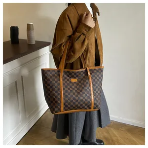 On-shoulder view of a large checkered tote bag with brown leather handles on a model