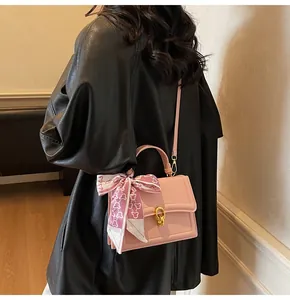 Detailed close-up of a pink leather crossbody bag with golden ring lock and silk scarf