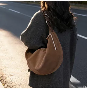 Dettaglio di una borsa a mezzaluna grande in camoscio marrone con zip argento sulla modella