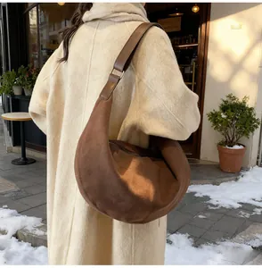 Borsa hobo in camoscio marrone indossata da una modella con cappotto di lana beige in strada
