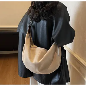 Dettaglio di una borsa a mezzaluna in camoscio kaki indossata su una giacca di pelle