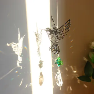 Detail of hummingbird crystal suncatcher with green beads casting rainbow light on wall