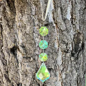 Detail of multi-layered green crystal suncatcher hanging on rustic dark tree bark