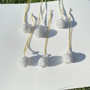 Detailed view of six white rhinestone Christmas ornaments with gold ribbons on white board