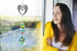 Suncatcher detail with silver angel wings and engraved heart pendant on a window