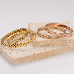 Detailed view of 18K gold and rose gold gear-edged bangles on beige stone