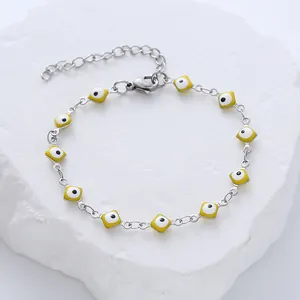 Silver steel bracelet with square yellow evil eye charms on white stone surface