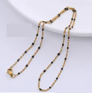 Elegante goldene Edelstahlhalskette mit kleinen schwarzen Perlen auf einer weißen Keramik