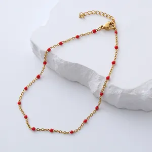 Detail of bohemian gold anklet with red beads on a textured stone surface