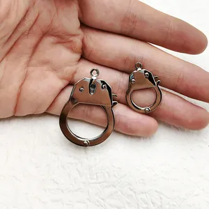 Detailed view of silver stainless steel handcuff charms held in hand for scale
