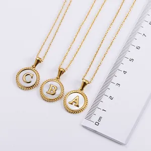Macro detail of 18k gold plated round letter pendants with white shell inlay and a ruler