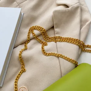Dettaglio della tracolla a catena dorata su borsa in pelle verde con elegante blazer
