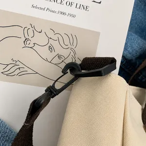 Detailopname van beige canvas stof met bruine katoenen band en een matzwarte metalen haak