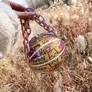 Detail of yellow basketball-shaped crossbody bag with graffiti and chunky purple chain