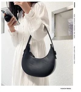 Fashionable black crescent shoulder bag held by a model in a white lace dress
