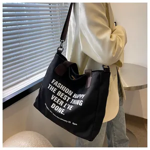 Detail van zwarte canvas shopper met witte typografie en bruine schouderriem