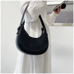 Close-up of minimalist black leather half-moon hobo bag styled with a white pleated dress