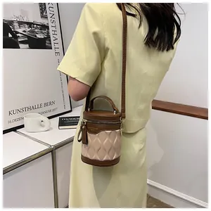 Detail of a contrast color bucket bag with leather stitching and metal logo on a model