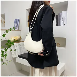 Detail of an ivory crescent leather bag with silver zipper hardware and slim shoulder strap