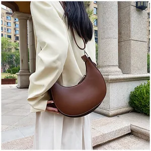 Close-up of brown half-moon shoulder bag in leather held by a model in outdoor setting