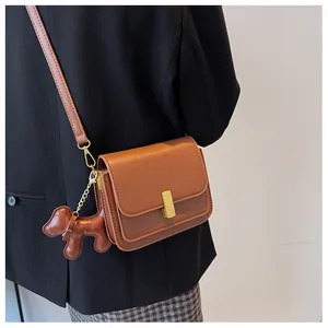 Close-up of brown rectangular crossbody bag with gold metal buckle and cute dog charm