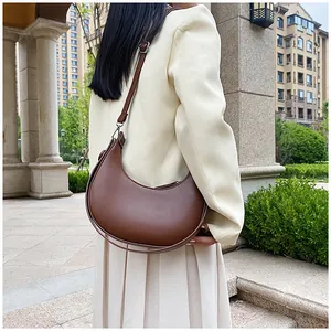 Brown leather half-moon shoulder bag styled with a beige suit in an outdoor setting