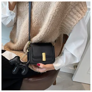 Detail of black crossbody bag with gold buckle and dog charm on a model outfit