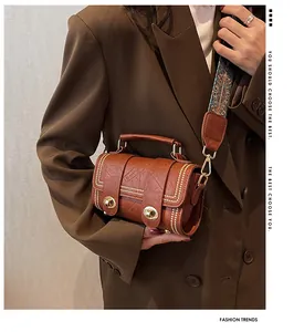 Brown cylinder crossbody bag with gold studs and vintage jacquard strap on a model