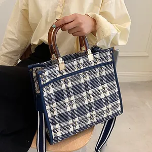 Detail of tweed tote bag showing wooden handle and adjustable striped canvas strap